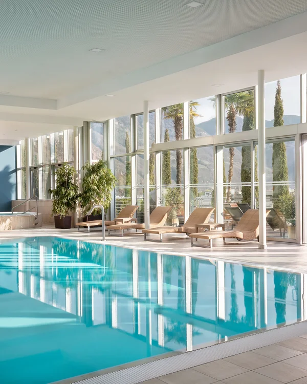 Modern indoor swimming pool with large windows and lounge chairs