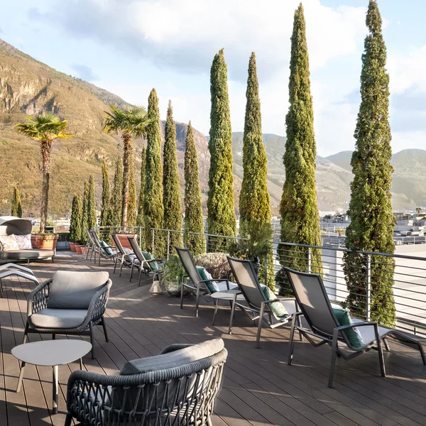 Terrasse mit Stühlen und hohen Bäumen neben einem Berg